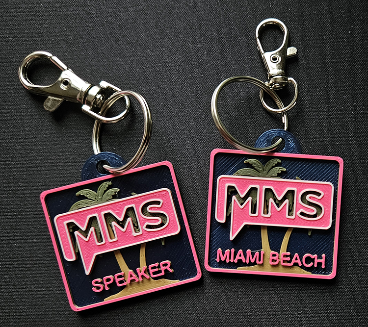 3D printed keyrings for MMS Miami Beach edition. Square five-color tags approximately 1.5 inches in size attached to metal key rings. The tags have a dark blue background, palm tree at center rear, "speaker" or "miami beach" text, and the MMS logo.